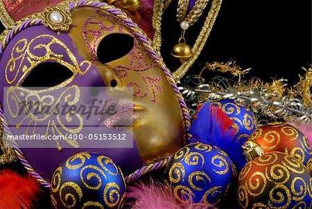 Beautiful Venetian mask on black background and christmas baubles with the similar golden motive