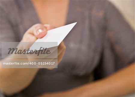 A woman is holding a piece of business card out in front of her.  Horizontally framed shot.