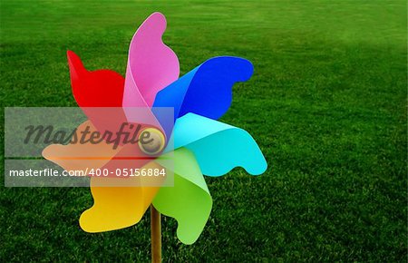 A multicolored pinwheel stands with a beautiful green grassy field