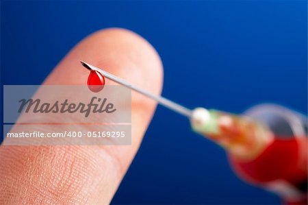 syringe needle with droplet of blood in front of a finger and on blue background