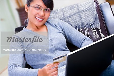 A young woman smiling to camera is about using her gold credit card for online transaction