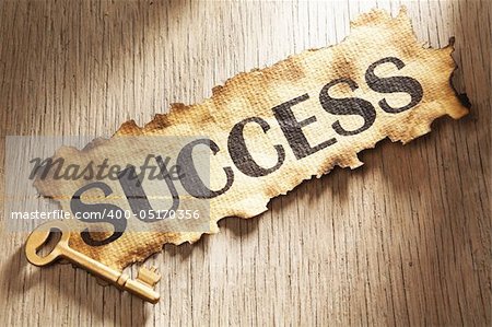 Key to success concept using burnt paper with word success printed on it and golden key placed on its side