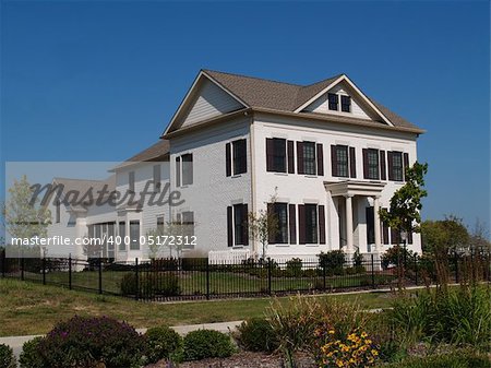 Two story new home built to look like an old historical home complete with the added on look, painted brick and a wrought  iron fence.