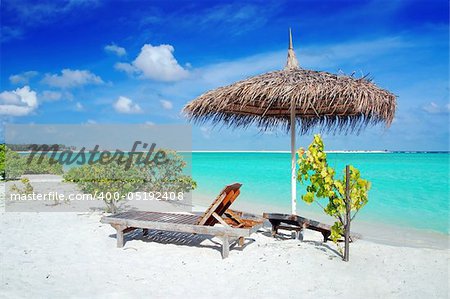 Beautiful Maldivian beach with parasol and two deck chairs in the front