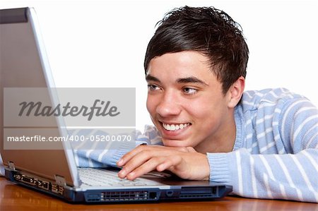 Young teenager is sitting on desk, is surfing on the internet and looking happy on laptop display. Isolated on white.