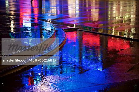 Red and blue neon lights reflected in puddles on the pavement (sidewalk, street)