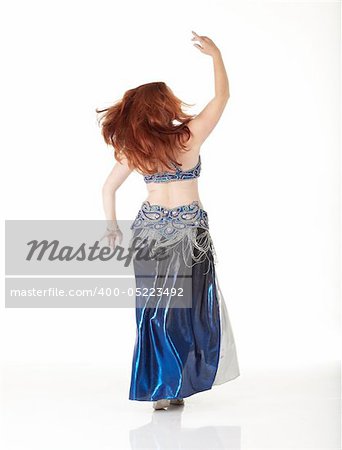 Lithe adult caucasian belly dancer with red hair and a blue belly dancing outfit performing steps on a white background. Not Isolated