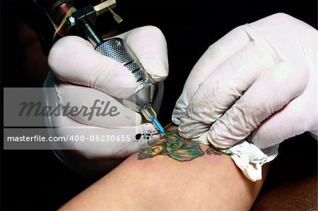 A tattoo artist applying his craft onto the hand of a female