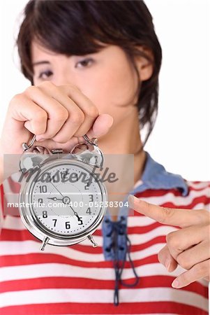 Woman holding alarm clock and pointing, time concept.