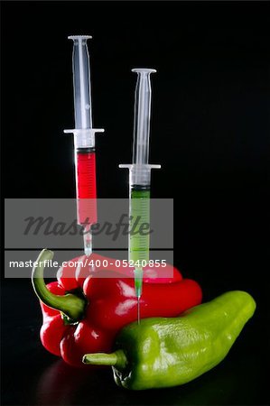 Injection with syringe to red and green peppers over black background