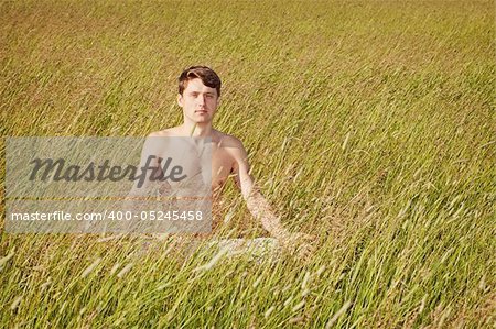 The man sits in a grass in a lotus pose