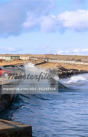 waves splashing against a coastal wall during a storm with cars and homes in background