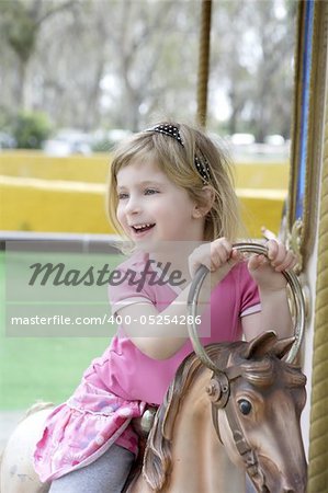 funny happy gesturing little blond girl playing on horses merry go round