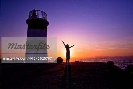 Beautiful landscape picture of a lighthouse and a woman looking the sunset