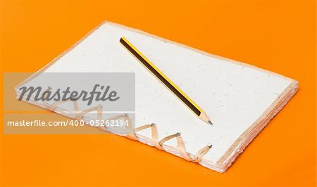 recycled notepad and pencil over an orange background