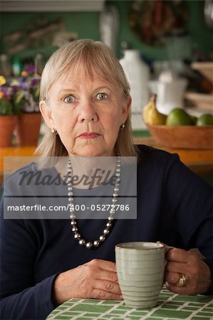 Depressed senior woman at home with coffee or tea