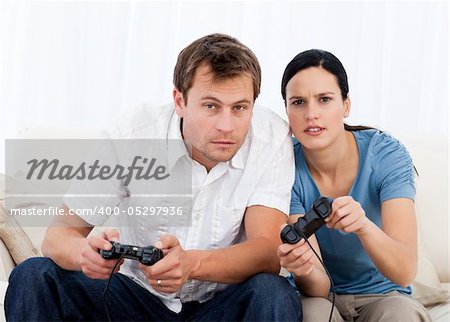 Concentrated couple playing video games together on the sofa at home