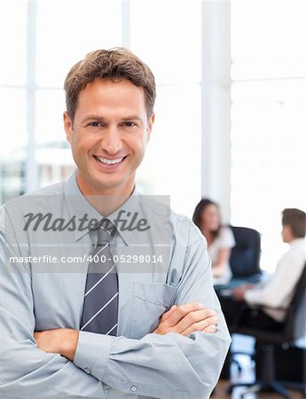 Happy businessman standing in front of his team while working at a table in the background