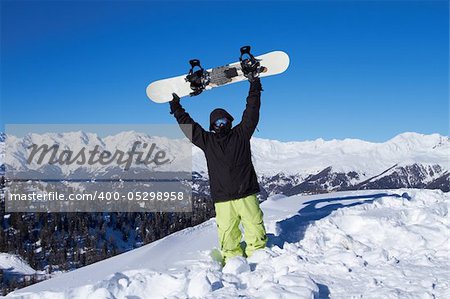 Snowboarder holding his snowboard over head