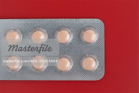 Close-up of a pack of orange pills on red background.