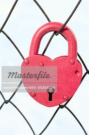 Padlock in form of the heart on net of the fence