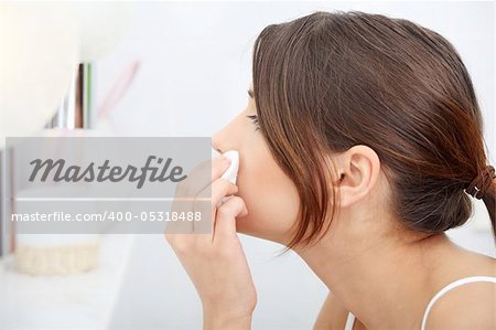 Young beautiful caucasian woman cleaning her face with cotton pad in the bathroom