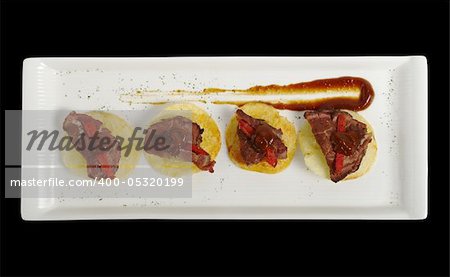 An appetizer of meat on potato chips with ketchup, photographed from above and isolated on black