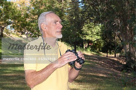 Healthy old man with binoculars engaged in his hobby of birdwatching in a wooded landscape.