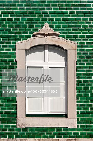 Traditional stone decorated window in a green tile background, Algarve, Portugal