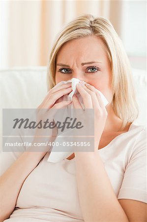 Portrait of a tired woman blowing her nose  in her lving room