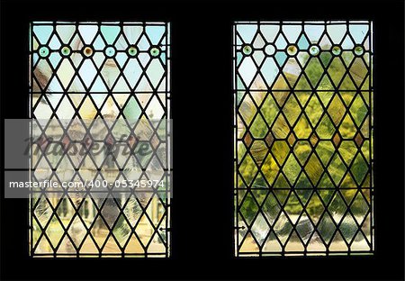 The view through two stained glass windows in the landmark Bruges Town Hall. The background of a building and tree in Burg Square is rendered in indistinct, almost impressionistic tones, through distortions from the old panes.