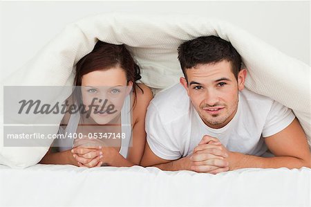 Happy couple hiding under their bvlanket in the bedroom