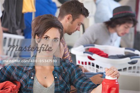 Serious Caucasian woman holding detergent and clothes in the laundromat