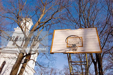 Old basketball board with an old tattered basketball net on the hoop near church.