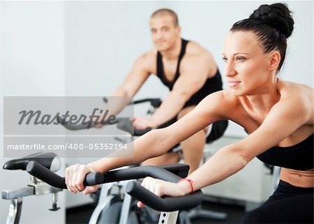 Young athletic couple spinning veloargometers in gym, female on focus