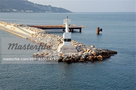 Áutomated lighthouse by the sea and rock jetty breakwater at port entrance.
