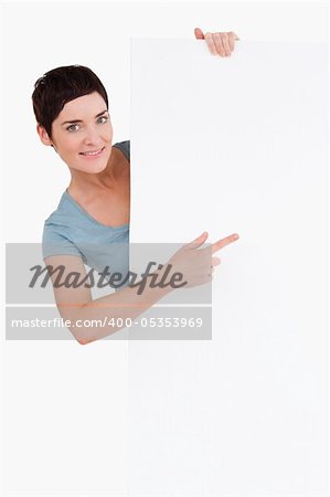 Beautiful brunette pointing at a blank panel against a white background