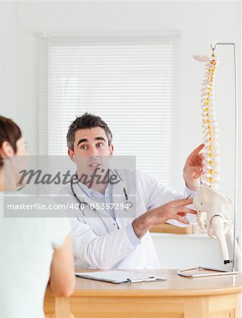 Male Doctor showing a female patient a part of a spine in a room