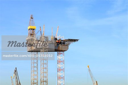 An oil rig is being constructed in a harbor area, to be towed to sea after completion.
