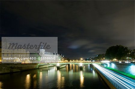 Bridges over the River Seine in Paris, with the Conciergerie on the Ile de la Cite nicely lit. A patch of clouds is lit with a lightbeam from below, just above the horizon