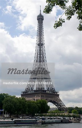 The famous landmark the Eiffel Tower seen from across the river Seine in paris, with the sun breaking through the clouds. The bus pariking is a tell tale for the masses who visit this world famous attraction