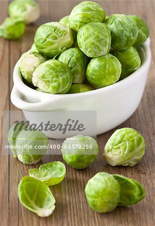 Brussels sprouts in a white ceramic saucepan on a wooden board.