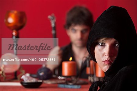 Serious witch stares with wizard holding sceptre over red background