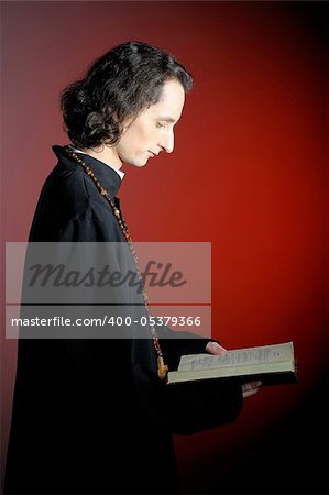 conceptual portrait of Praying priest with wooden cross reading Holy Bible. red background