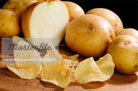 Onion flavored extra crispy potato chips with potatoes and onions in the background over black