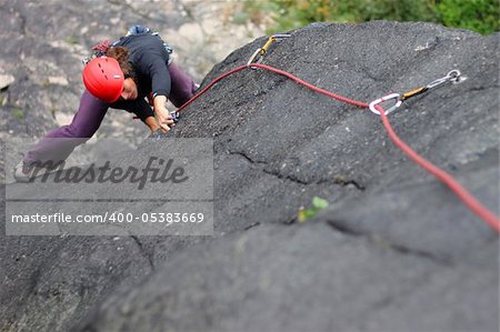 Young woman with helmet climbing basalt rock