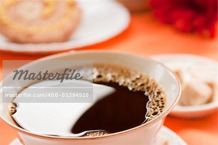 Coffee in white cup  with cake in the back. Focus is on the front bubbles.
