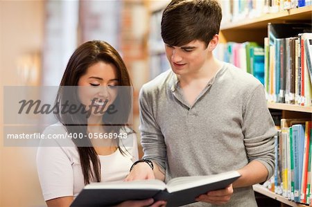Happy students looking at a book in a library