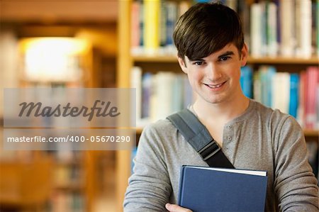 Smiling young student holding a book in a library