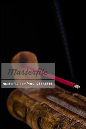 A burning incense stick on a handcrafted burner